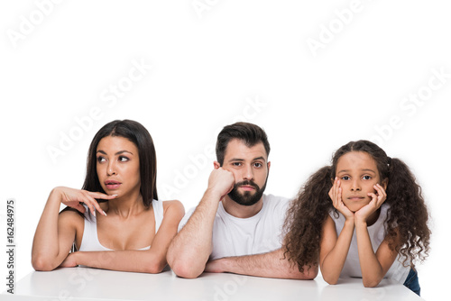 Pensive multiethnic family sitting together with hands on faces isolated on white