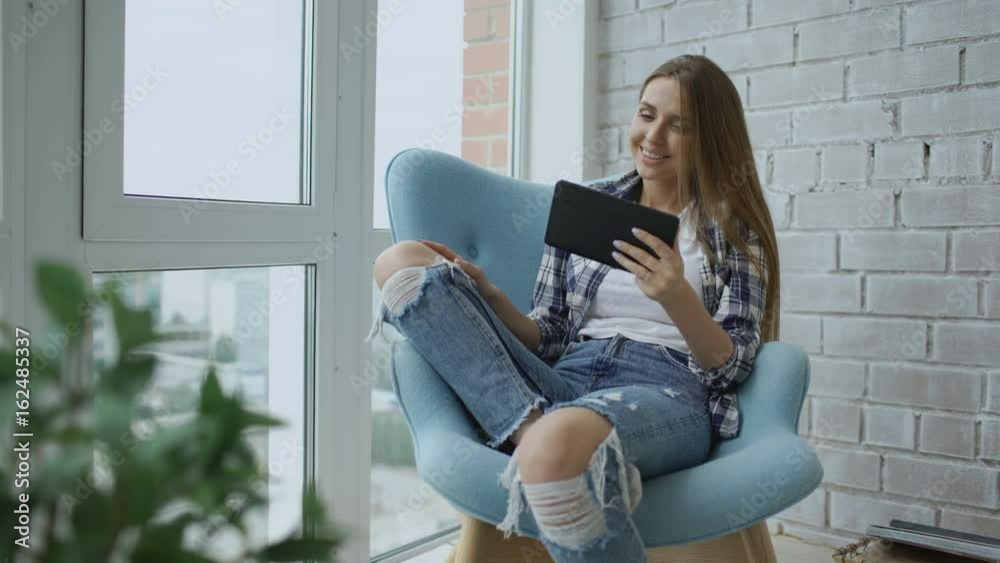 Young smiling woman have online video chat using digital tablet computer sitting on balcony in modern loft apartment
