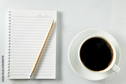 White cup of coffee morning on wooden table with notebook