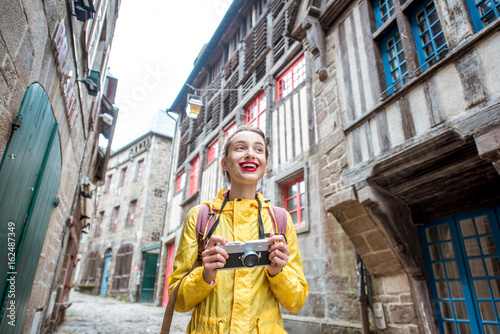 Young woman in yellow raincoat walking with backpack and photo camera in Dinan village at Brittany region in France