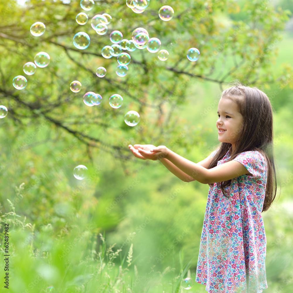 Cute little girl on a forest glade among lush vegetation and around fly soap bubbles. Kid wih soap bubbles over nature outdoor. Cute little girl on a forest glade among lush vegetation and around fly soap bubbles. Kid wih soap bubbles over nature outdoor.