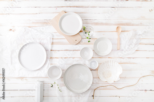 Set of different ceramic plates and bowls styled on white distressed wooden background. Flat lay with copy space