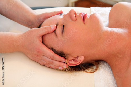 Massage of head and face in spa center. Massage wellness studio. Happy young woman enjoying face and collar area massage getting spa treatment in salon. Facial energy massage. Body and health care.