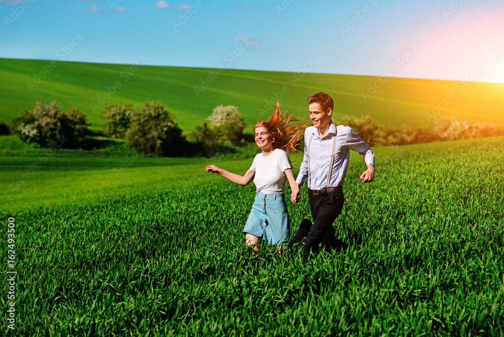 Young happy lovers running on meadow with green grass and blue sky Young happy lovers running on meadow with green grass and blue sky