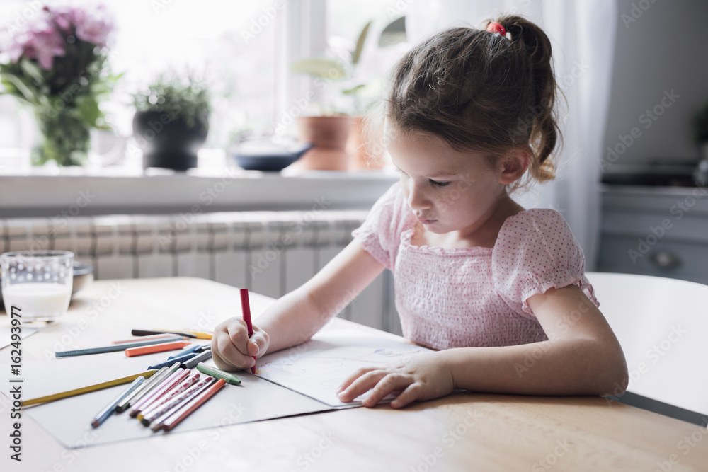 Cute little Caucasian girl drawing with crayons on kitchen table. Cute little Caucasian girl drawing with crayons on kitchen table.
