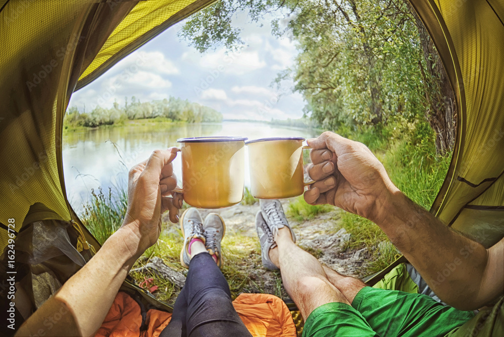 Young couple sitting   in the tent and drinking tea while looking on the Desna river , Ukraine - obrazy, fototapety, plakaty 