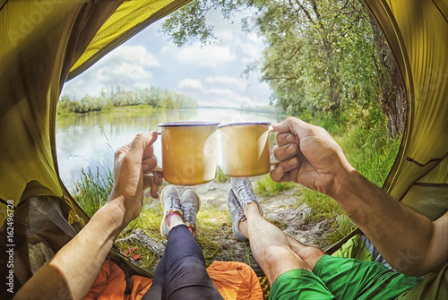 Young couple sitting   in the tent and drinking tea while looking on the Desna river , Ukraine