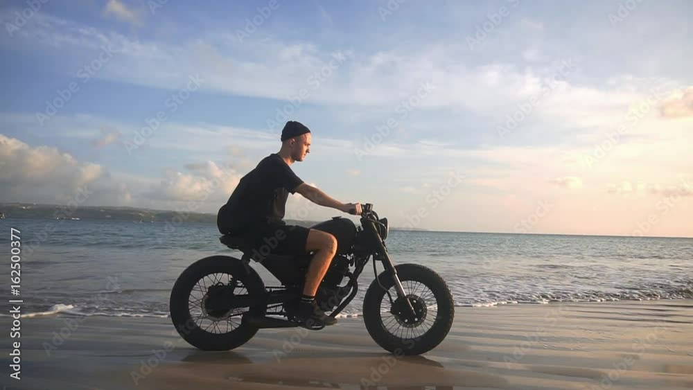 Motorcyclist driving his motorbike on the beach during sunset Motorcyclist driving his motorbike on the beach during sunset