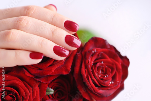 Hands of a woman with red manicure with a bouquet of red roses. Close up