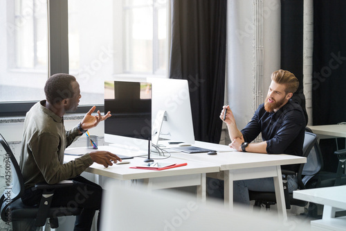 Two young male colleagues sitting at opposing desks