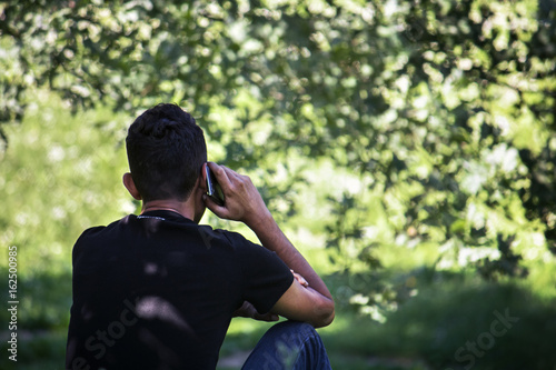 man using telephone at park, blurred and green foliage background