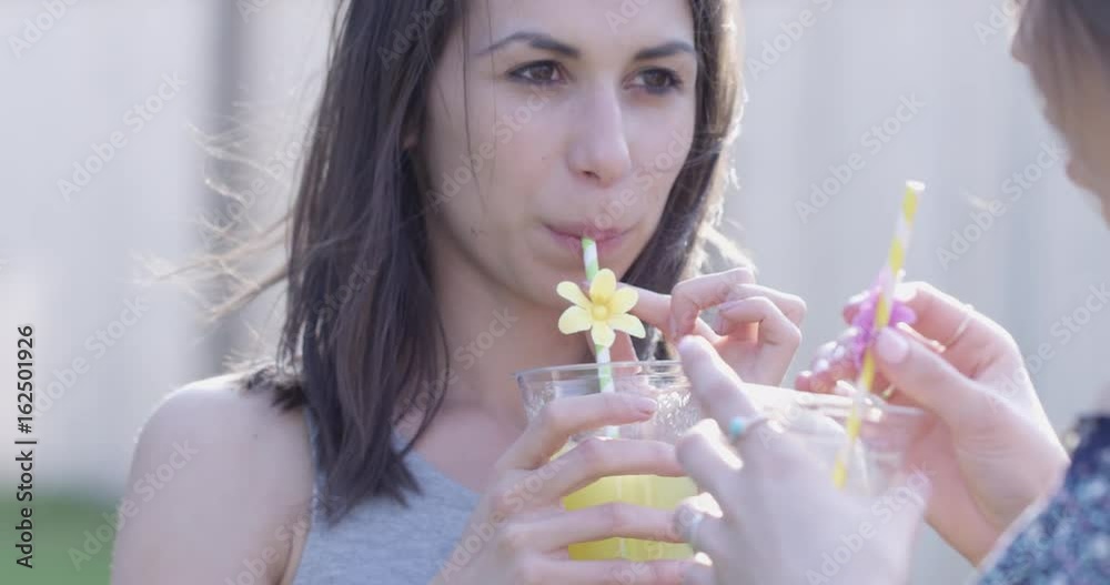 Attractive young women sip cocktails and chat outdoors summer - slow motion Attractive young women sip cocktails and chat outdoors summer - slow motion