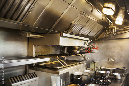 Interior view of restaurant kitchen, pots on stovetop, grill and extractor hood.