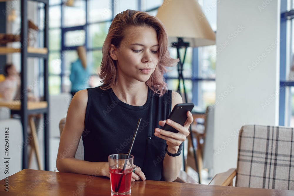 Attractive woman using smartphone and drinking a cocktail in a cafe.