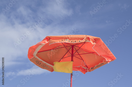 An orange umbrella with a yellow flag of lifeguard