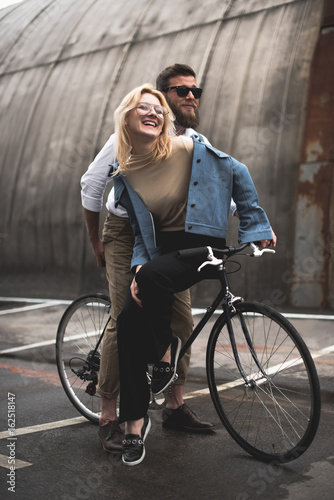 stylish cheerful young couple riding bicycle on parking place