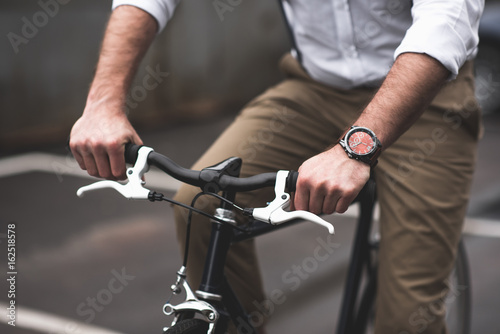 cropped view of stylish young man with watch riding bicycle