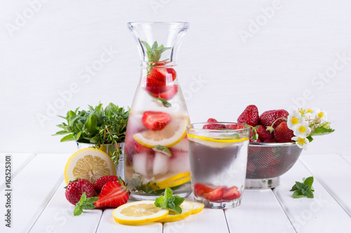 Mineral infused water with strawberry, ice, herb and mint leaves on white background, homemade detox soda water recipe.