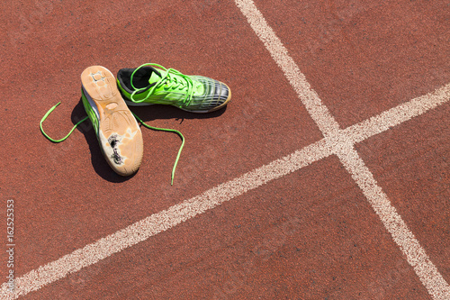 Konstfotografi A pair of broken green running shoes with big holes in the sole laying on a runn