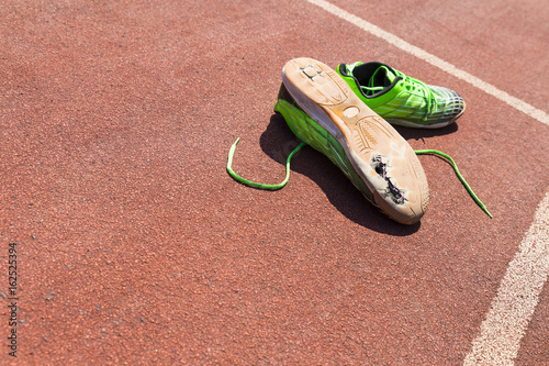Konstfotografi A pair of broken green running shoes with big holes in the sole laying on a runn