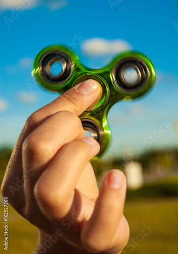 Quadro su tela Hand holding popular green fidget spinner toy on sky background