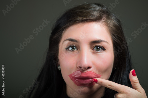 Beautiful natural girl woman pointing with her hand to her face a lips pink mask, spa treatments. Cosmetology in a dark background photo