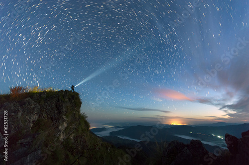 Star trail over the mountain with the man light up the sky before sunsire, Nan Province, Thailand © narathip12