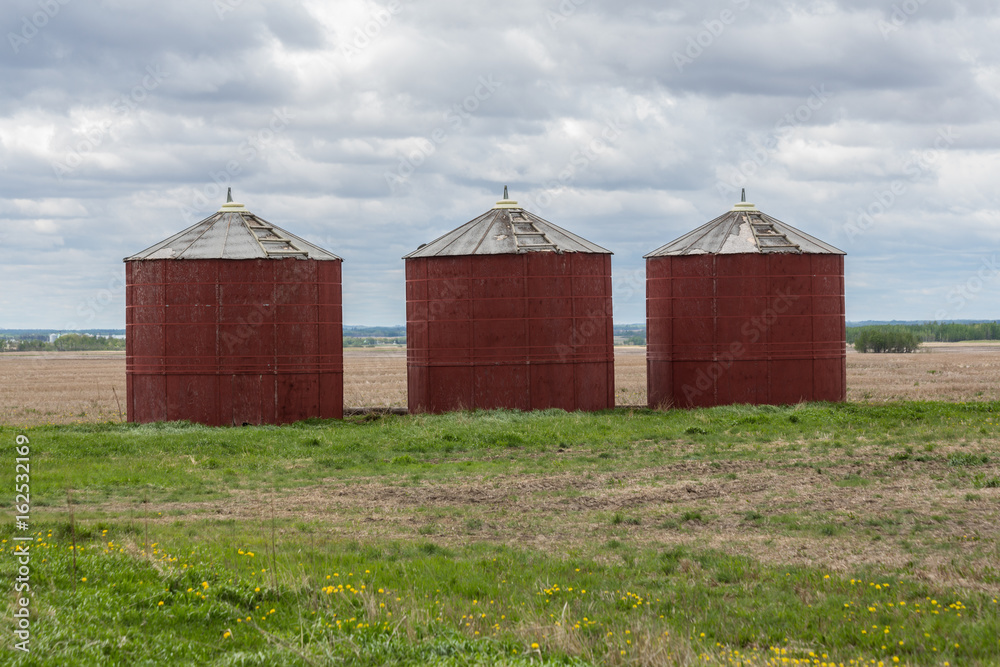 three red wooden grain bins with cloudy skies three red wooden grain bins with cloudy skies