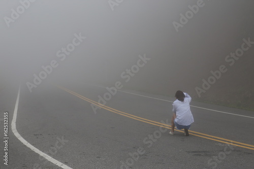 The woman sitting on the road which have a fog