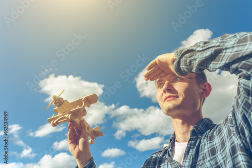 Young handsome man holding wooden airplane in hand and looking into the distance. Dreamer concept