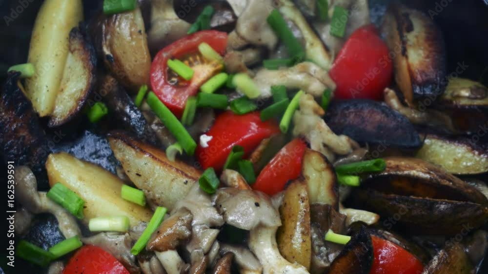Frying potato with mushroom, tomato and onion in butter using a frying pan. Preparing food on campfire in wild camping.
