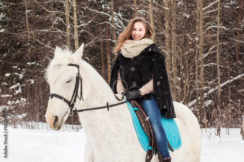 Nice girl and white horse outdoor in snowfall in a winter