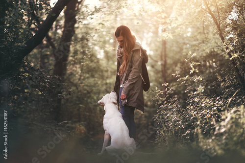 Junge Frau mit jungem labrador retriever hund welpen im wald bei sonnenuntergang