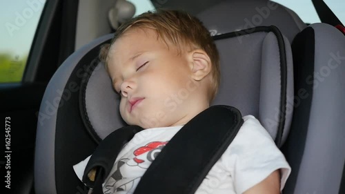 The baby sleeps in the car in the way. Sleeping child at back chair in car in slow motion.