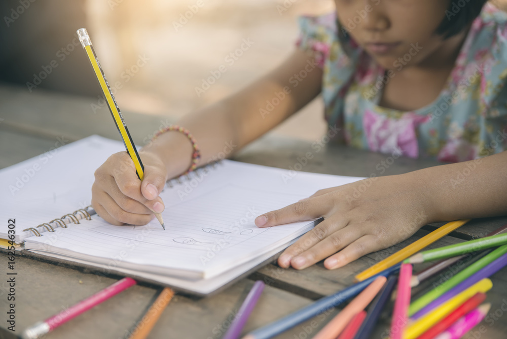 Adorable little girl doing homework,bored or tired asian kid writing on paper.Little Child hate doing homework,stress child for exam,colored pencils on wooden desk Adorable little girl doing homework,bored or tired asian kid writing on paper.Little Child hate doing homework,stress child for exam,colored pencils on wooden desk