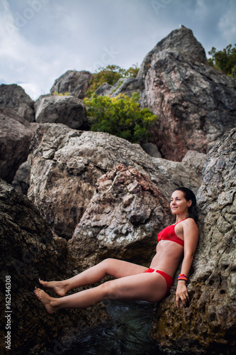 the girl in the red swimsuit on a rocky seashore