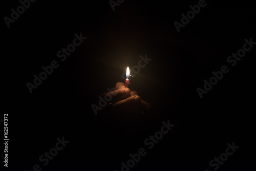 Hand holding burning candle in the dark photo