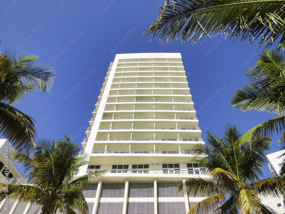 White modern apartment building with palm trees and blue sky.