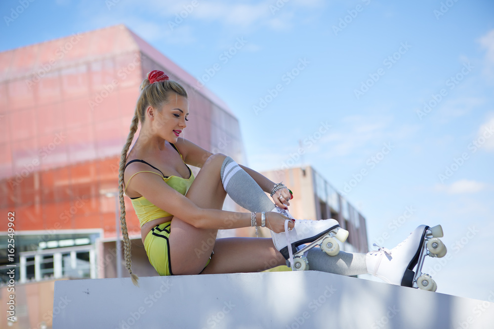  blond girl on roller skates sitting in a city park  of the river. Sunny summer day in Europe.