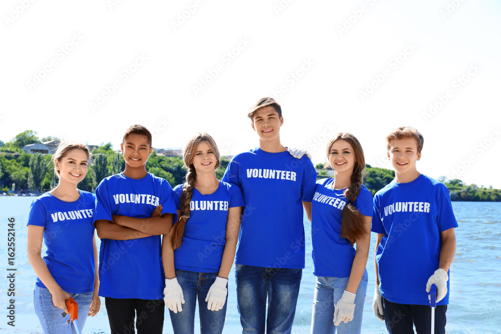 Obraz premium Young people with trash pickers standing on beach near river. Volunteer concept