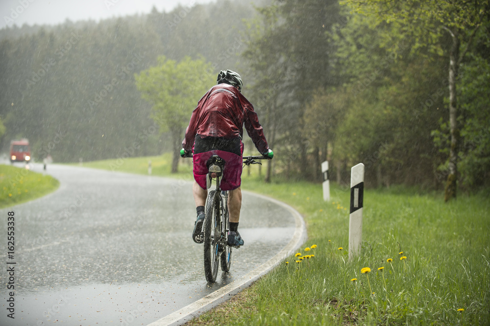 Obraz premium Mann fährt auf dem Fahrrad im strömenden Regen einen Anstieg hinauf