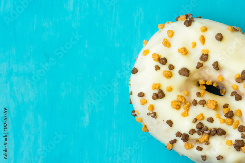 White glazed doughnut with chocolate and caramel sprinkles in right bottom corner on light blue background, copyspace, template, birthday, card, poster, top view, macro