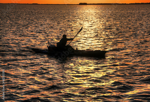 fisherman in small boat silhoette, orange sunset © Joel