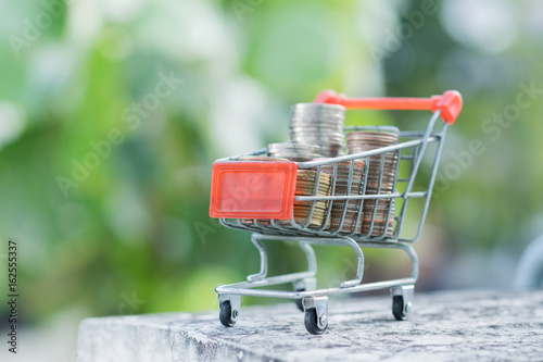 e-commerce  saving and shopping concept. Stack of coins in mini shopping cart with green nature background.