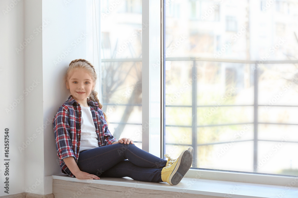 Smiling girl sitting on sill near big window Smiling girl sitting on sill near big window