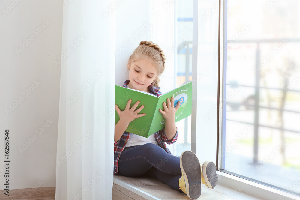 Small girl reading book on sill near window Small girl reading book on sill near window
