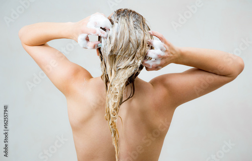 Woman washing her blond hair with shampoo