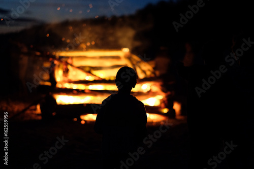 Silhouette of a child against the background of a large fire at the celebration of the summer solstice. Latvia.