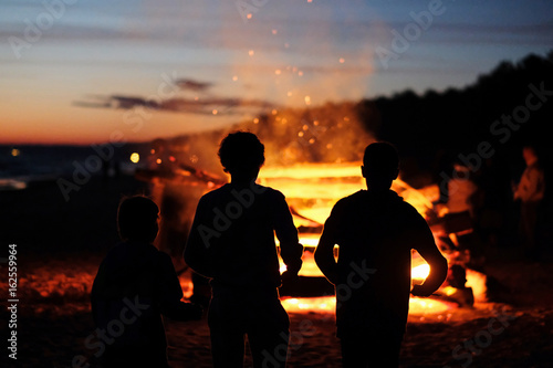 Silhouettes of children against the background of a large fire at the celebration of the summer solstice. Latvia.