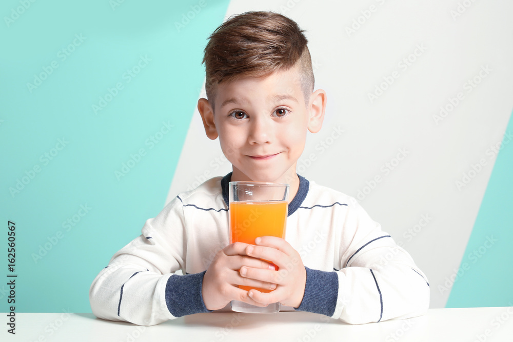 Cute little boy with glass of juice sitting at table, on color background Cute little boy with glass of juice sitting at table, on color background